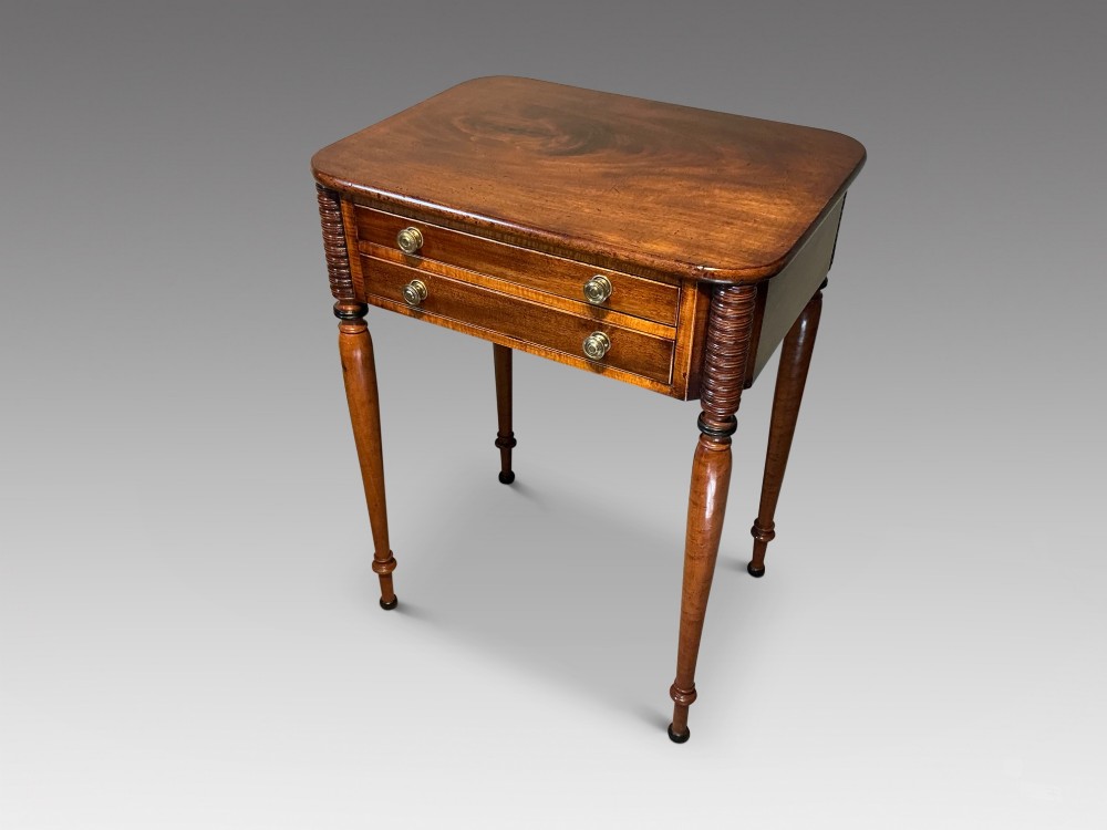 An early nineteenth-century mahogany and maple work table featuring two drawers with brass knobs, reeded upper corner detailing, and turned legs.