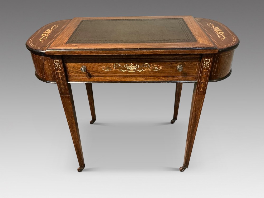 An antique inlaid rosewood writing table featuring a dark leather inset surface, classical urn marquetry, a single drawer, and square tapered legs on brass castors.