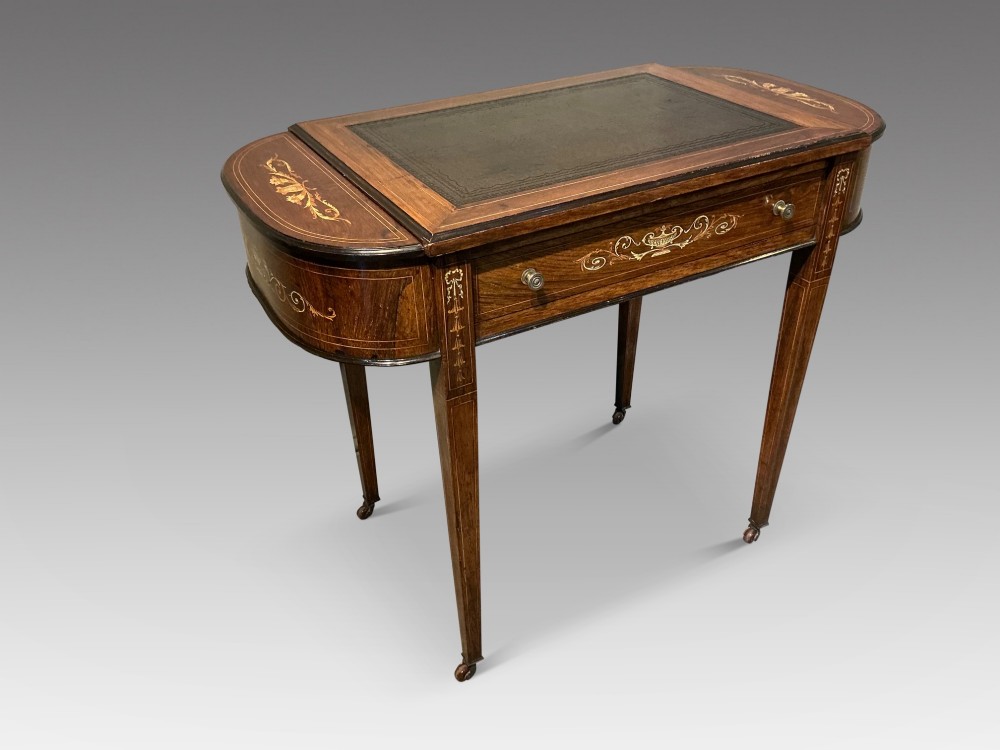 An antique inlaid rosewood writing table featuring a dark leather inset surface, classical urn marquetry, a single drawer, and square tapered legs on brass castors. View II
