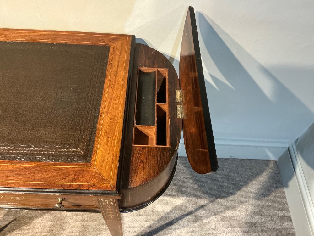 An antique inlaid rosewood writing table featuring a dark leather inset surface, classical urn marquetry, a single drawer, and square tapered legs on brass castors. View IV