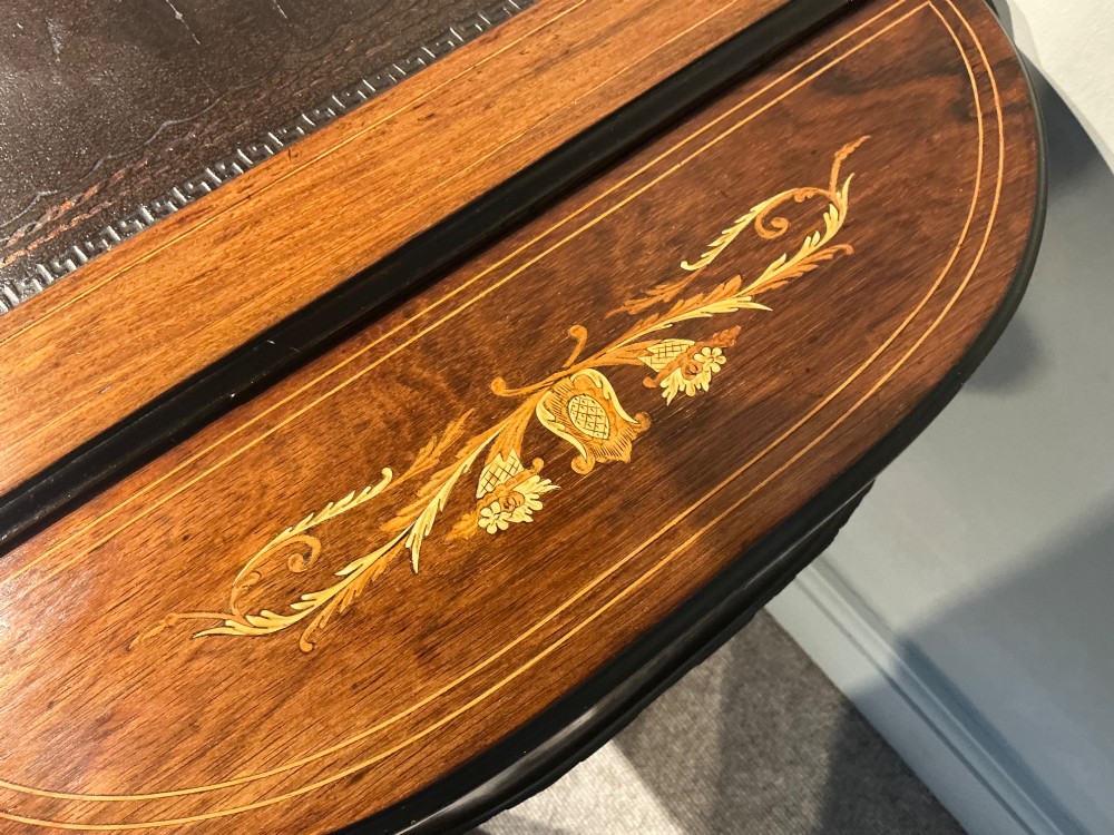 An antique inlaid rosewood writing table featuring a dark leather inset surface, classical urn marquetry, a single drawer, and square tapered legs on brass castors. View VI