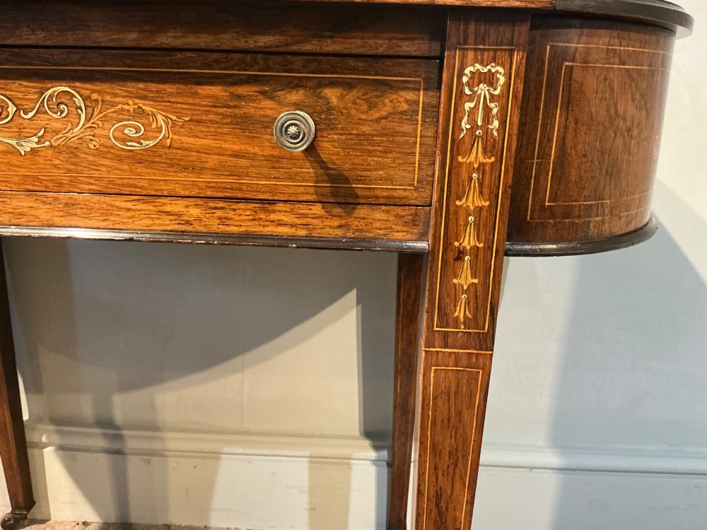 An antique inlaid rosewood writing table featuring a dark leather inset surface, classical urn marquetry, a single drawer, and square tapered legs on brass castors. View VIII