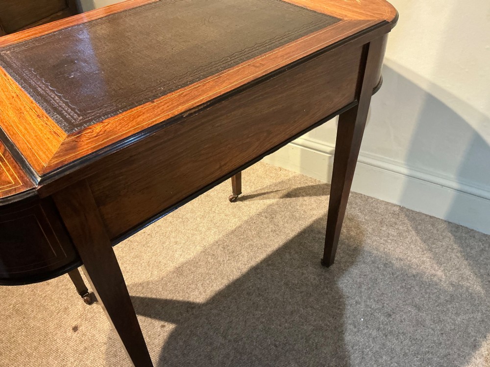 An antique inlaid rosewood writing table featuring a dark leather inset surface, classical urn marquetry, a single drawer, and square tapered legs on brass castors. View XI