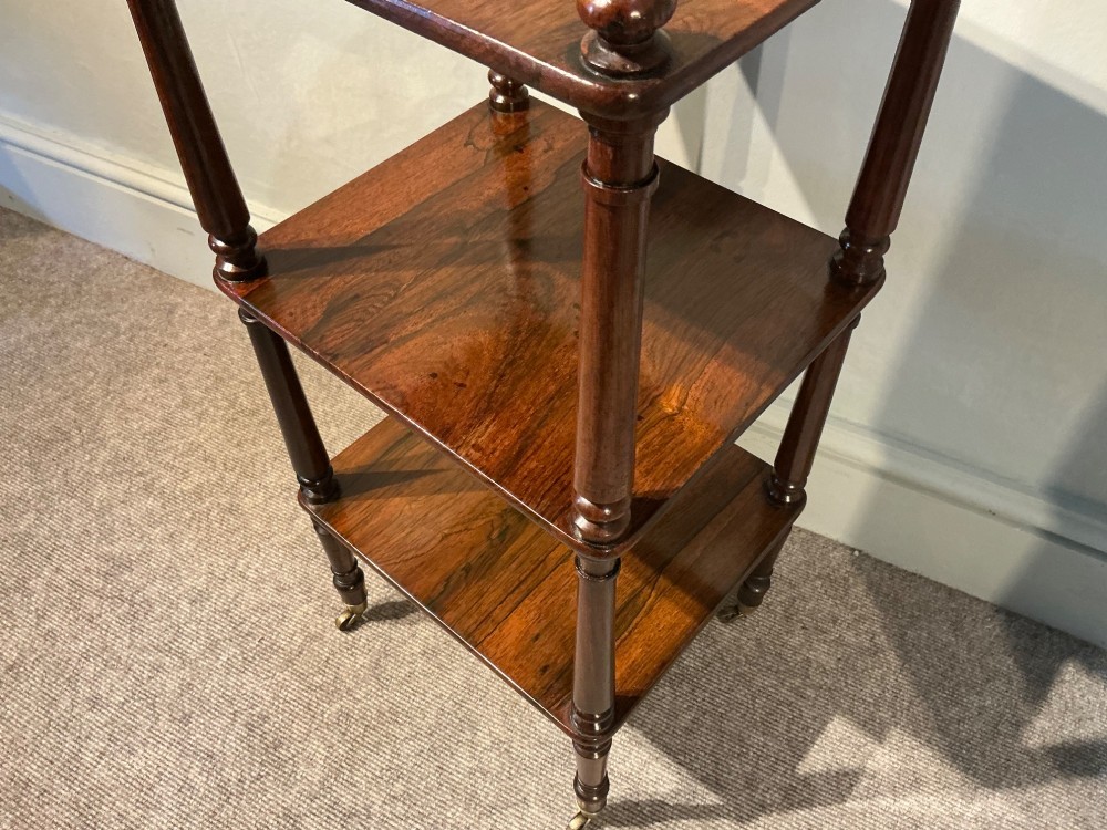 A three-tiered dark rosewood Regency etagere featuring turned supports, corner finials, and brass castors. View IV