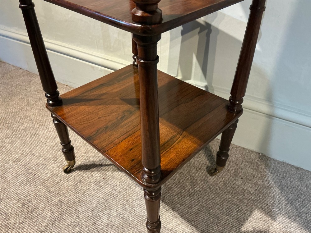 A three-tiered dark rosewood Regency etagere featuring turned supports, corner finials, and brass castors. View V