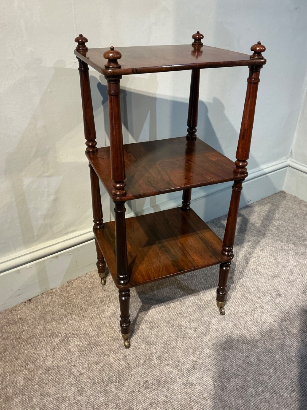A three-tiered dark rosewood Regency etagere featuring turned supports, corner finials, and brass castors. View VI