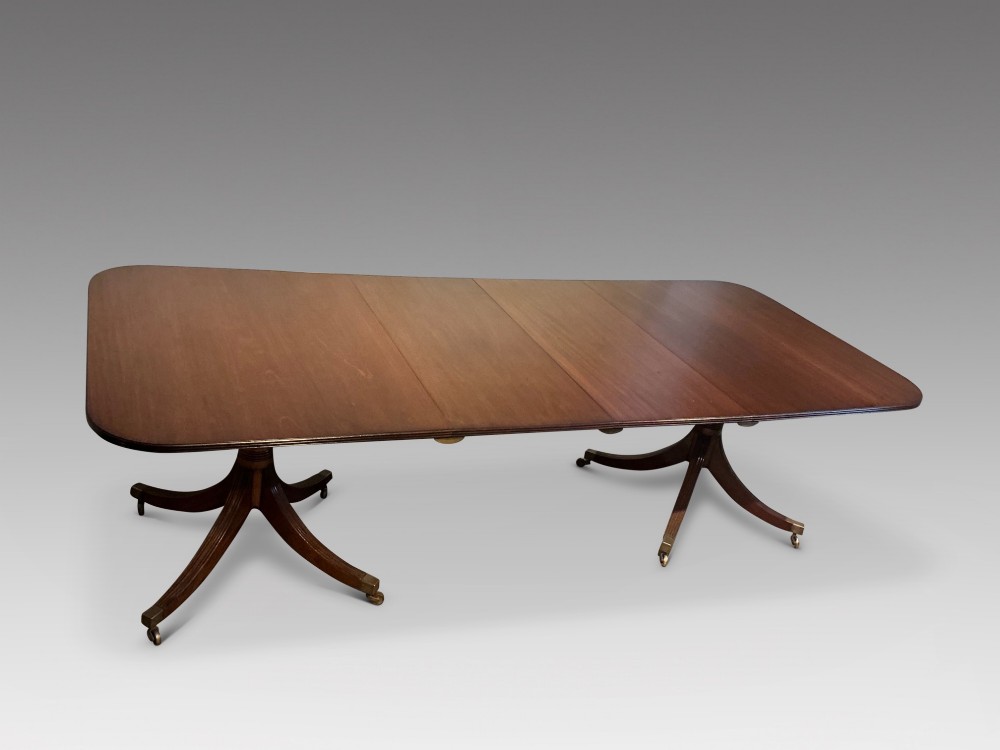 A mahogany twin pedestal dining table featuring rounded rectangular top corners, splayed tripod legs, and brass castors. View II