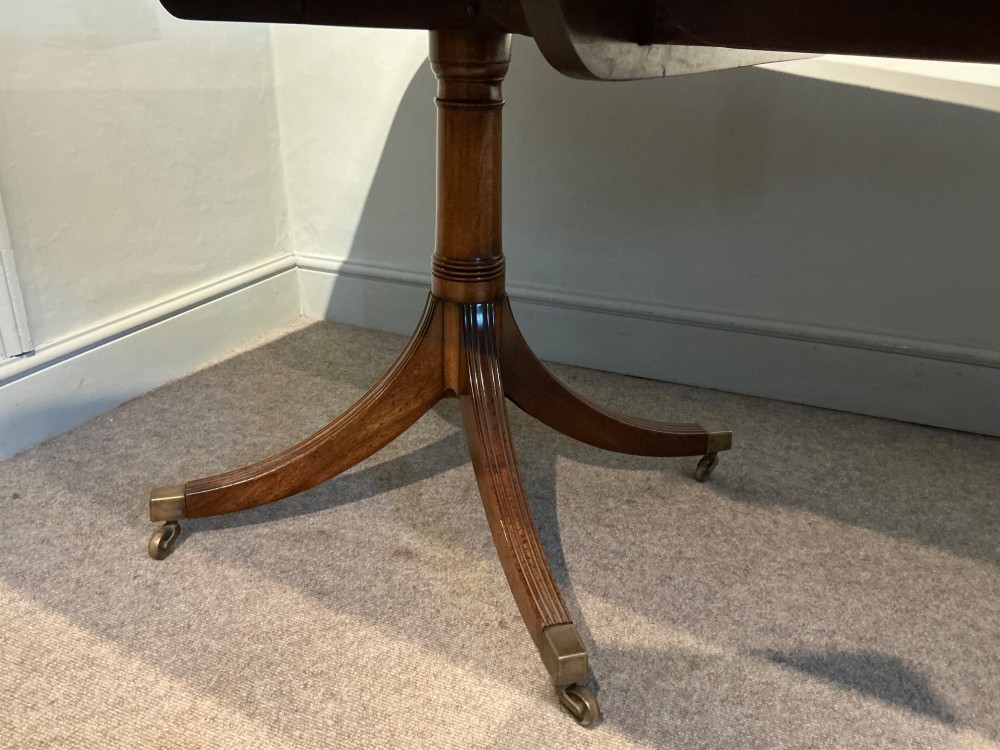 A mahogany twin pedestal dining table featuring rounded rectangular top corners, splayed tripod legs, and brass castors. View VII