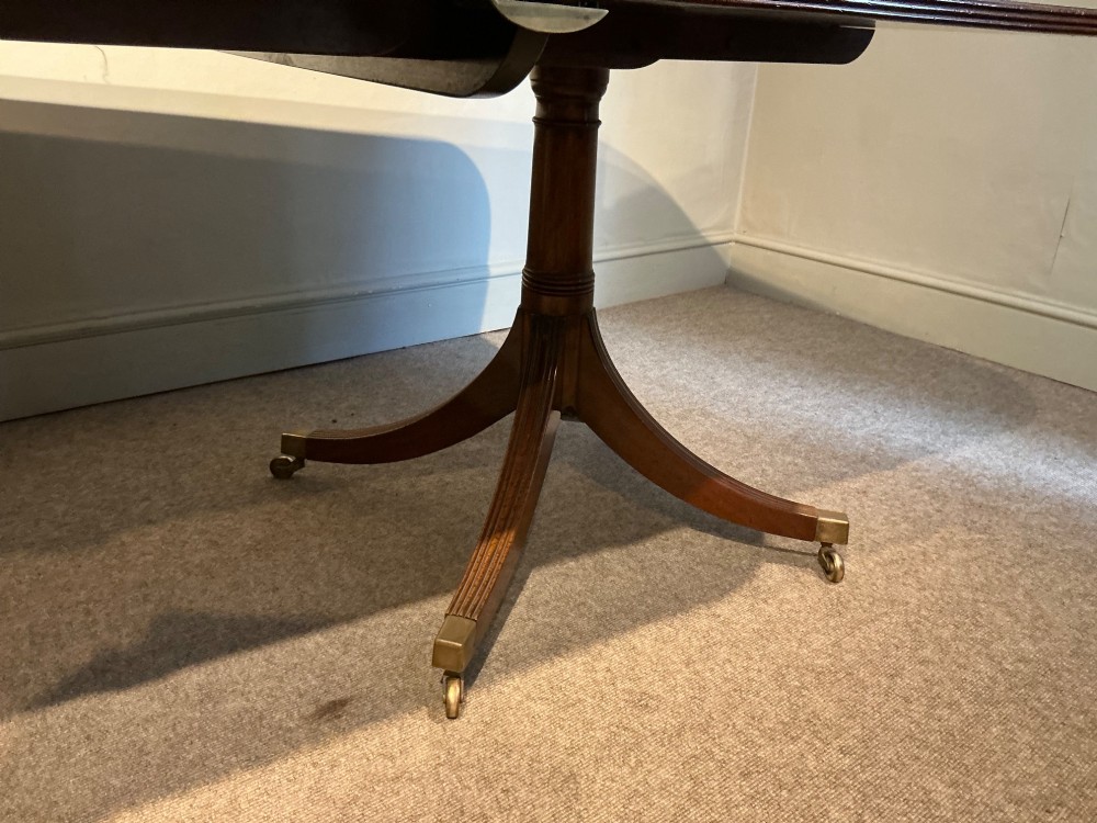 A mahogany twin pedestal dining table featuring rounded rectangular top corners, splayed tripod legs, and brass castors. View VIII