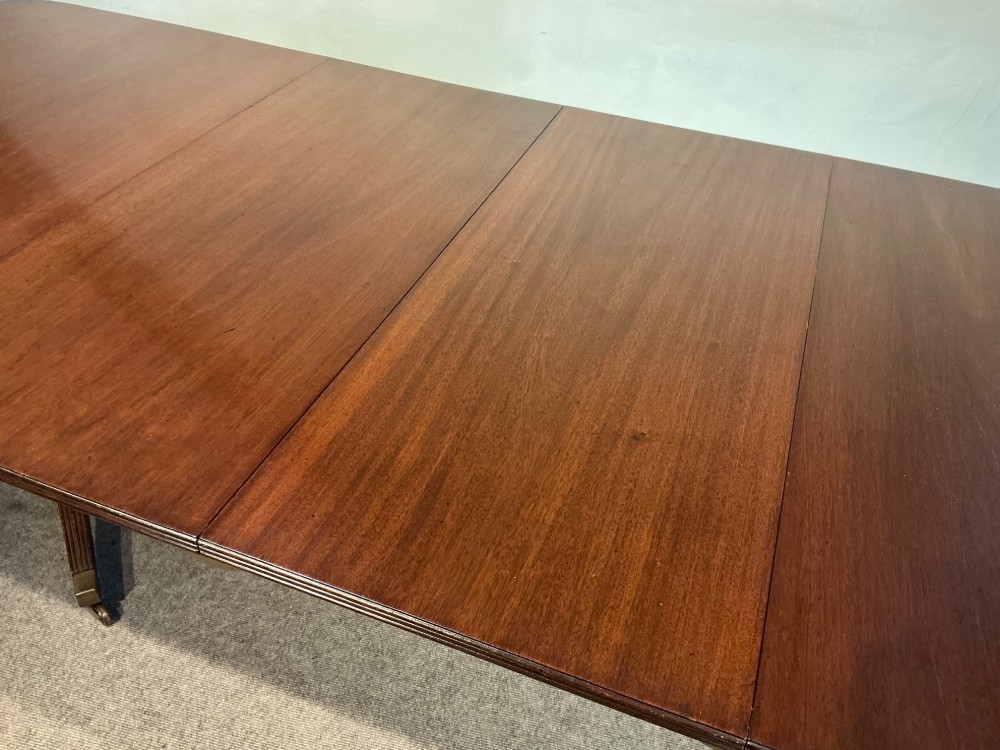 A mahogany twin pedestal dining table featuring rounded rectangular top corners, splayed tripod legs, and brass castors. View X