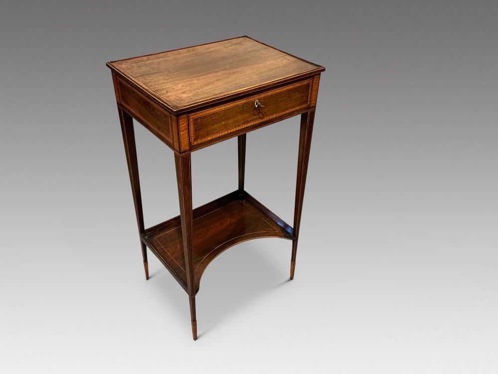 A late Georgian Sheraton mahogany work table featuring satinwood crossbanding, a single drawer, tapered square legs, and a concave lower undertier.