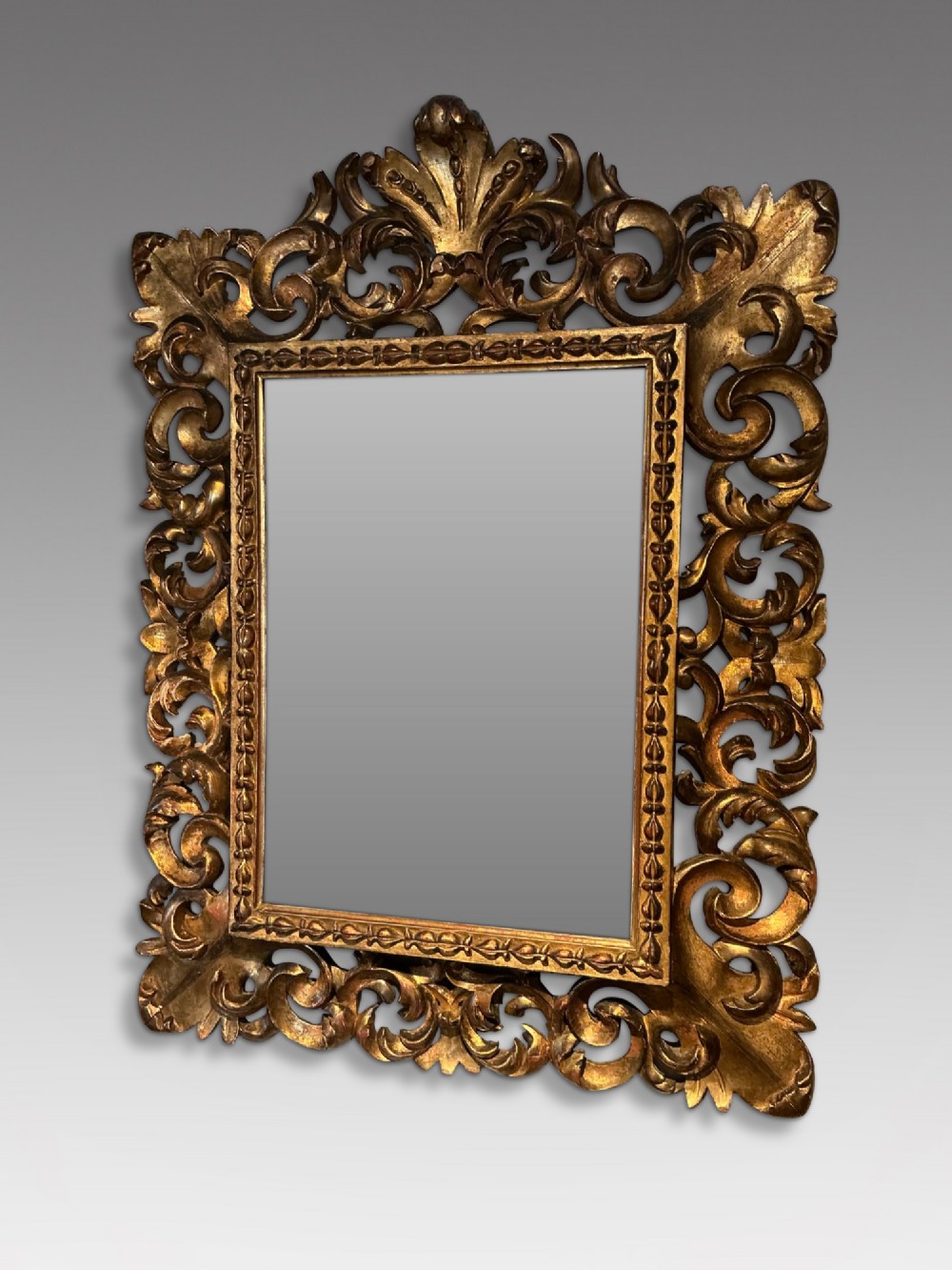 A rectangular antique wall mirror featuring a heavily carved and pierced giltwood frame decorated with acanthus leaf motifs and scrollwork.