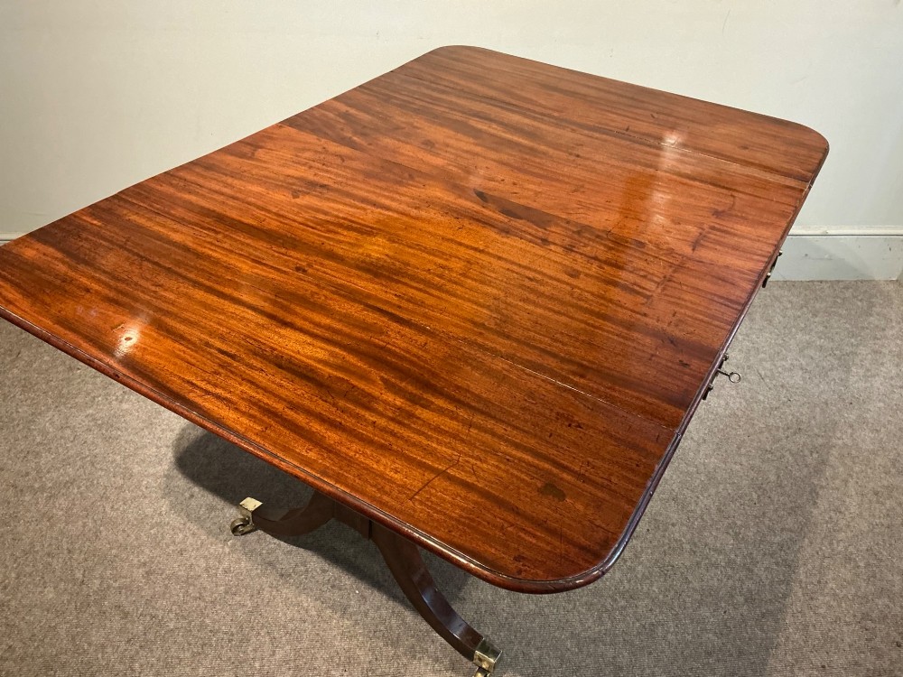 An antique Georgian mahogany sofa table with two drop leaves, two front drawers with brass handles, and splayed legs resting on brass castors. View VIII