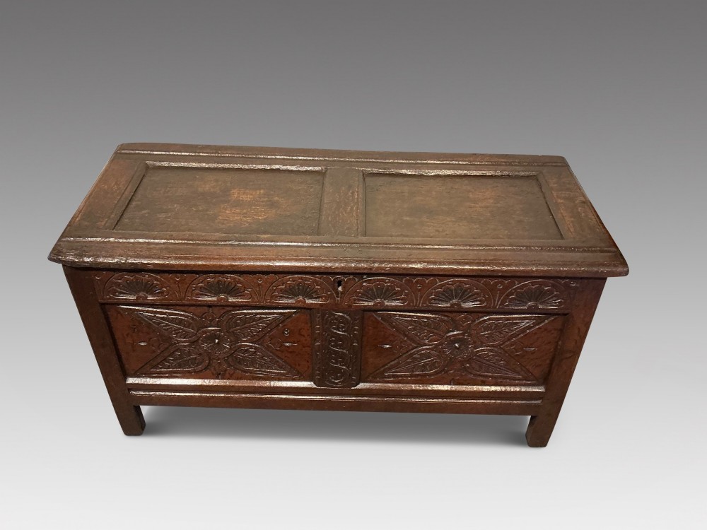 A dark oak coffer featuring hand-carved floral panels and a hinged two-panel top lid. View II