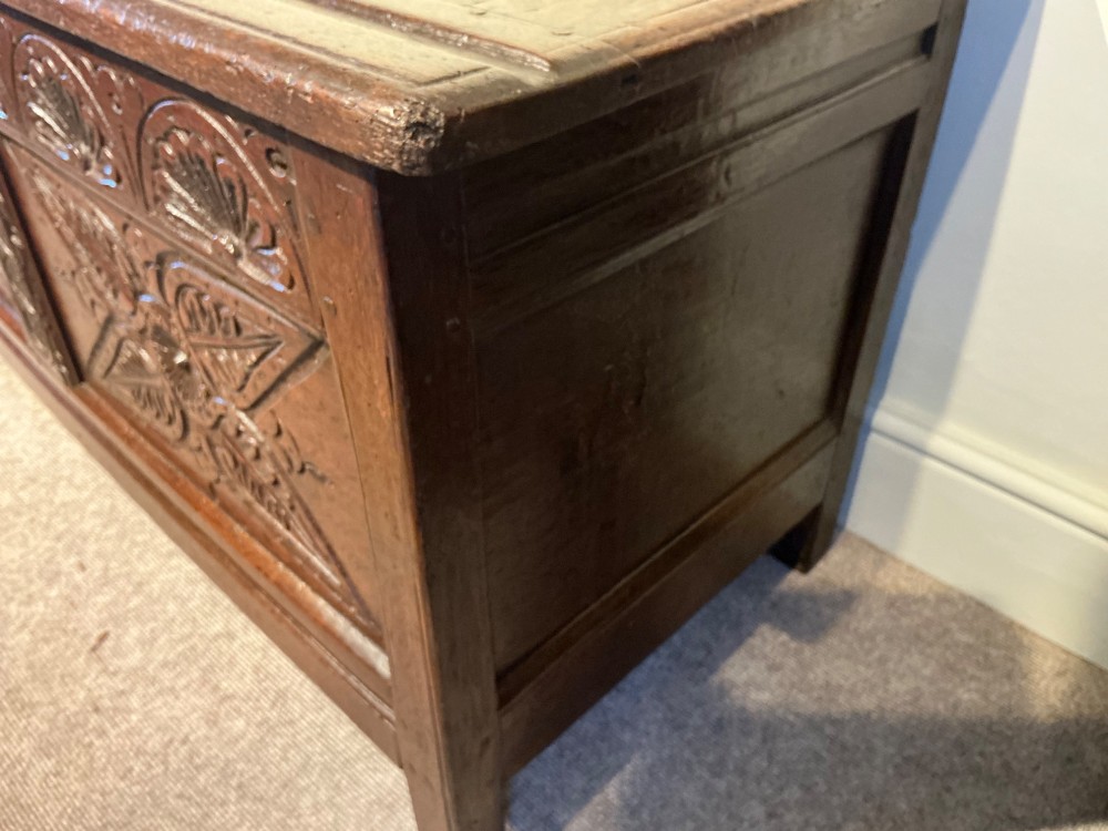 A dark oak coffer featuring hand-carved floral panels and a hinged two-panel top lid. View V
