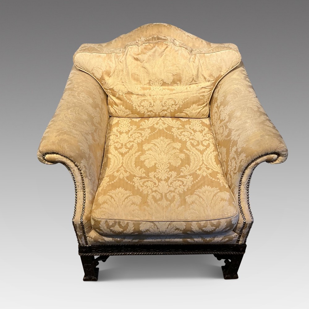 A deep upholstered armchair with gold damask fabric, broad scroll arms with brass stud trim, and carved dark timber legs. View II