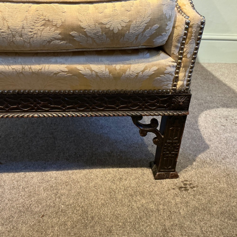 A deep upholstered armchair with gold damask fabric, broad scroll arms with brass stud trim, and carved dark timber legs. View III