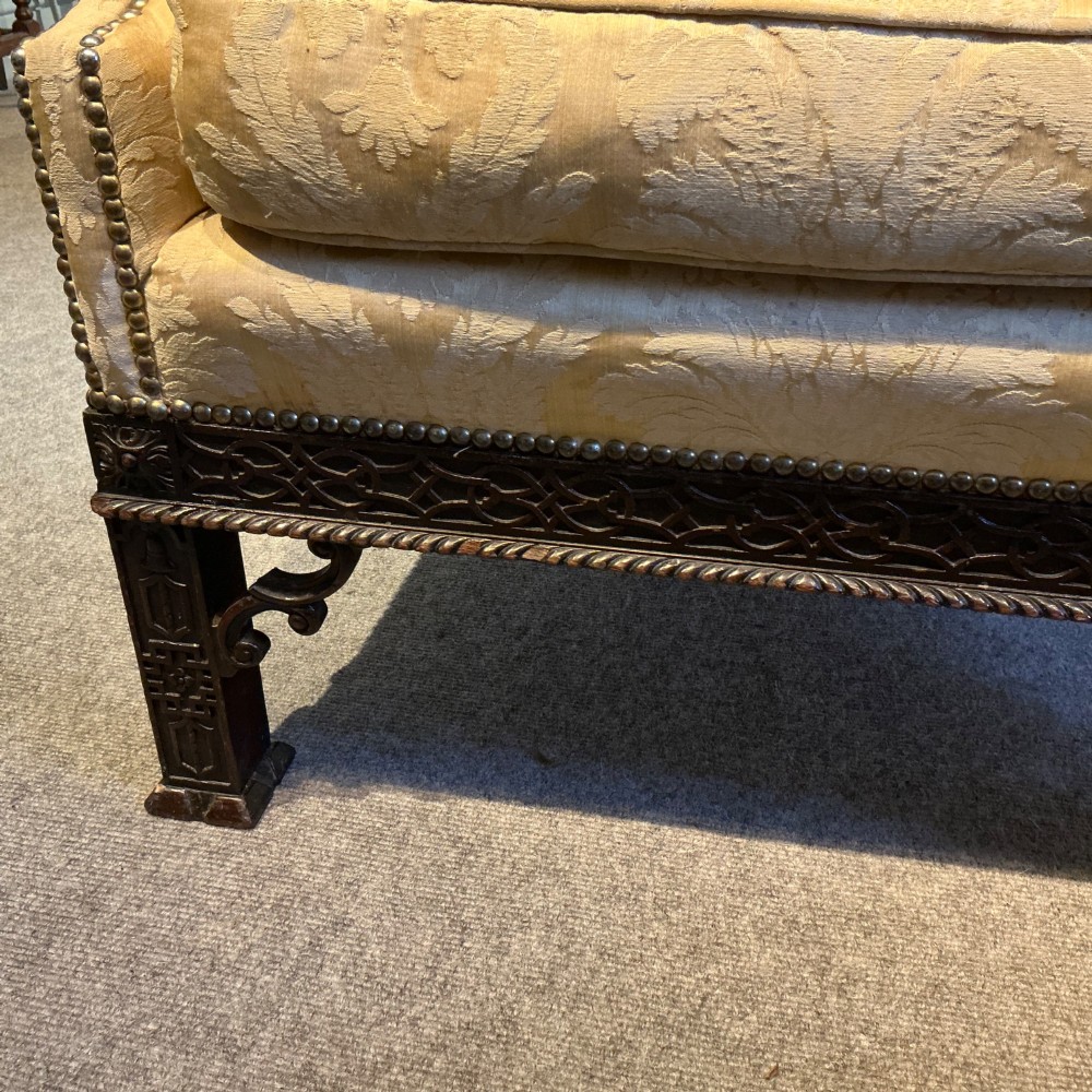 A deep upholstered armchair with gold damask fabric, broad scroll arms with brass stud trim, and carved dark timber legs. View IV