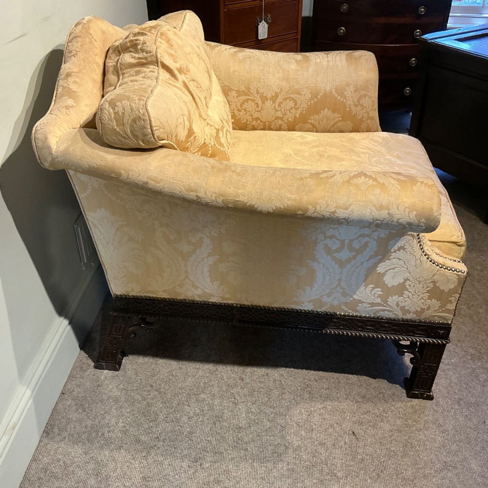 A deep upholstered armchair with gold damask fabric, broad scroll arms with brass stud trim, and carved dark timber legs. View V