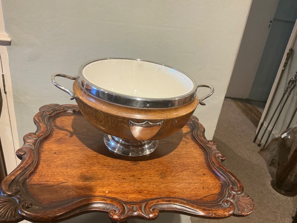 An Edwardian turned oak bowl featuring a silver-plated rim, twin loop handles, a pedestal foot, a blank shield cartouche, and a white ceramic liner. View II