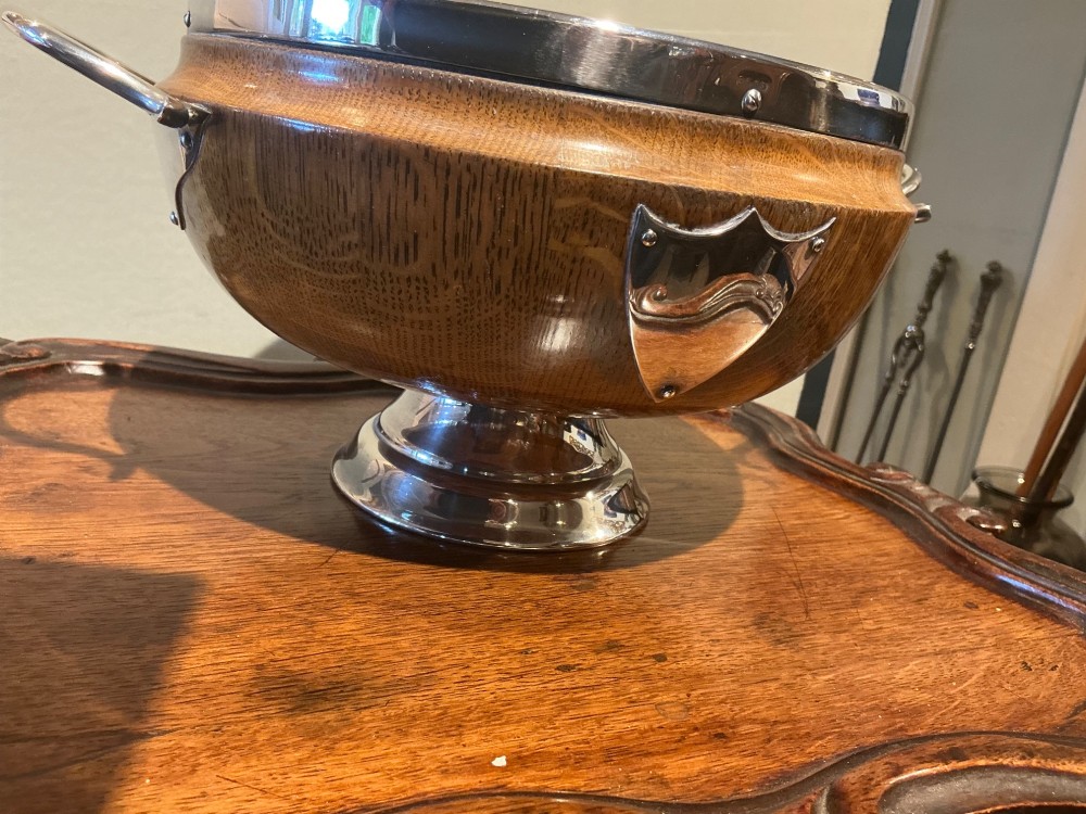 An Edwardian turned oak bowl featuring a silver-plated rim, twin loop handles, a pedestal foot, a blank shield cartouche, and a white ceramic liner. View III