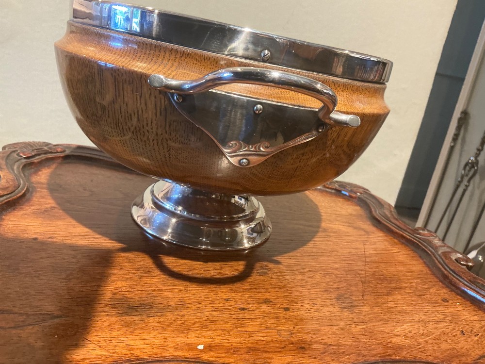 An Edwardian turned oak bowl featuring a silver-plated rim, twin loop handles, a pedestal foot, a blank shield cartouche, and a white ceramic liner. View IV