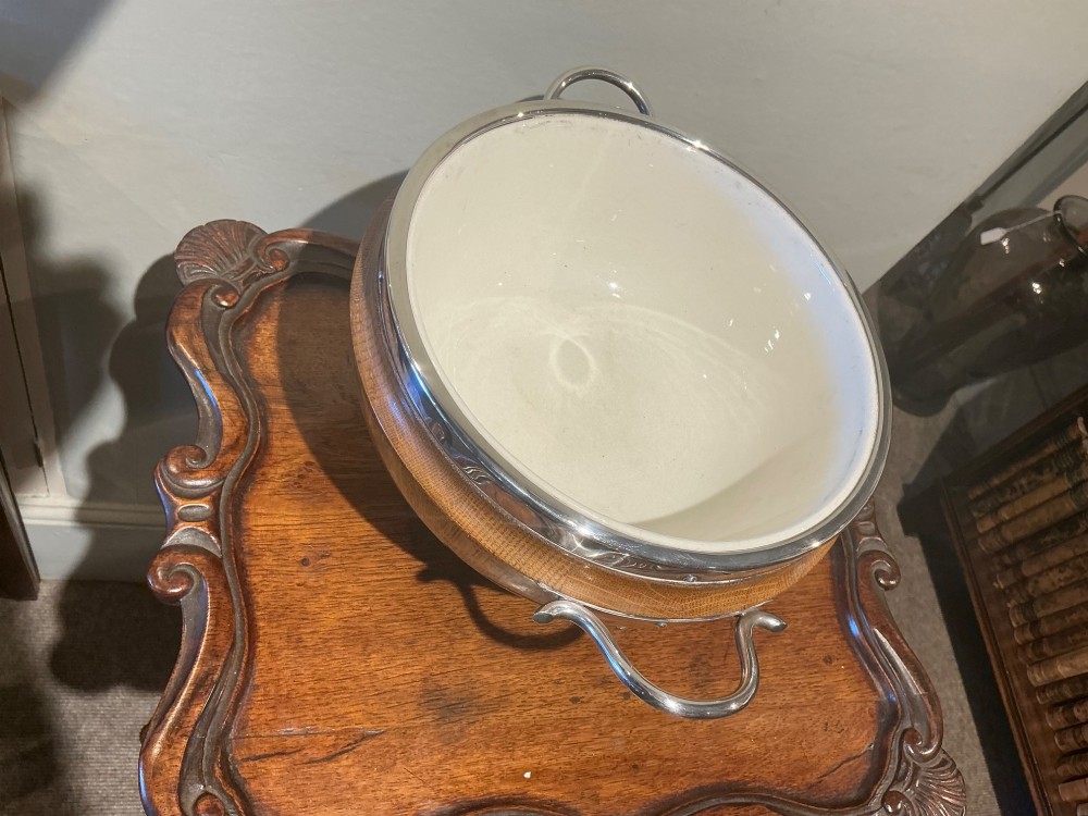 An Edwardian turned oak bowl featuring a silver-plated rim, twin loop handles, a pedestal foot, a blank shield cartouche, and a white ceramic liner. View V