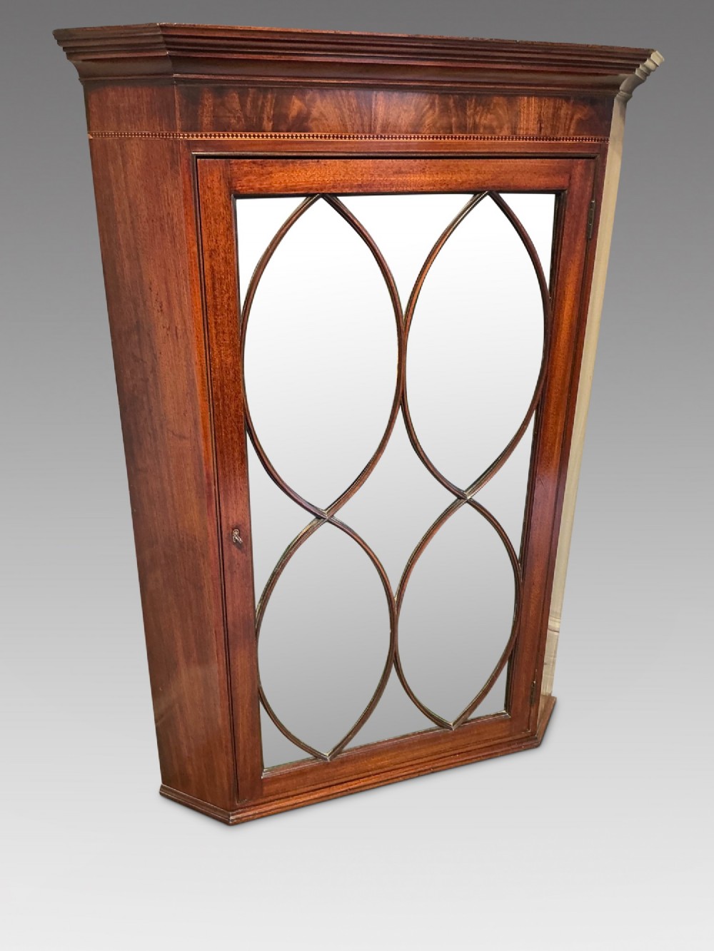 A Georgian mahogany wall-hanging corner cabinet featuring a moulded cornice and a single glass door with geometric oval astragal glazing bars.