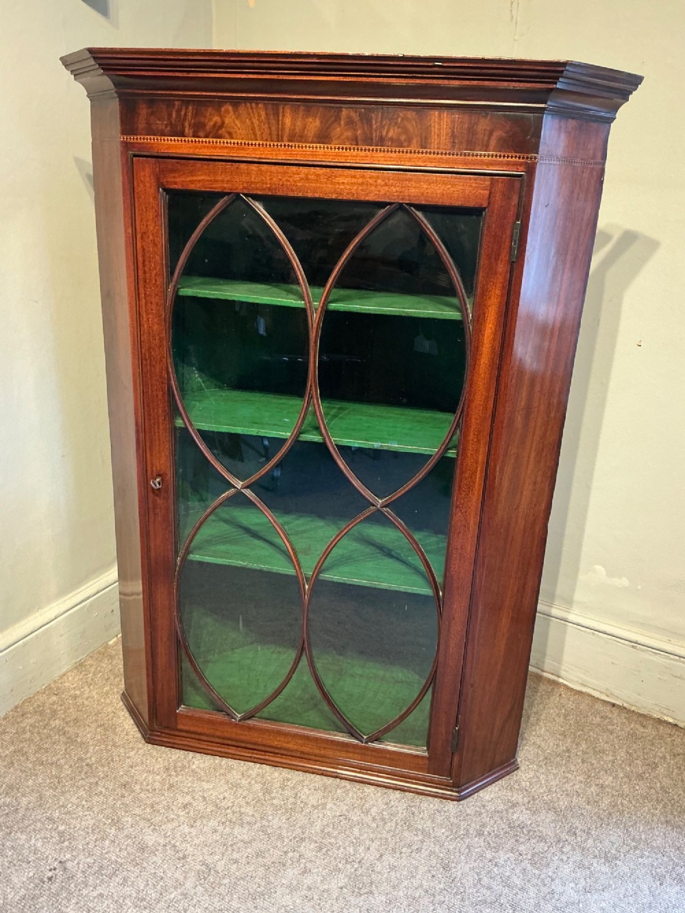 A Georgian mahogany wall-hanging corner cabinet featuring a moulded cornice and a single glass door with geometric oval astragal glazing bars. View II