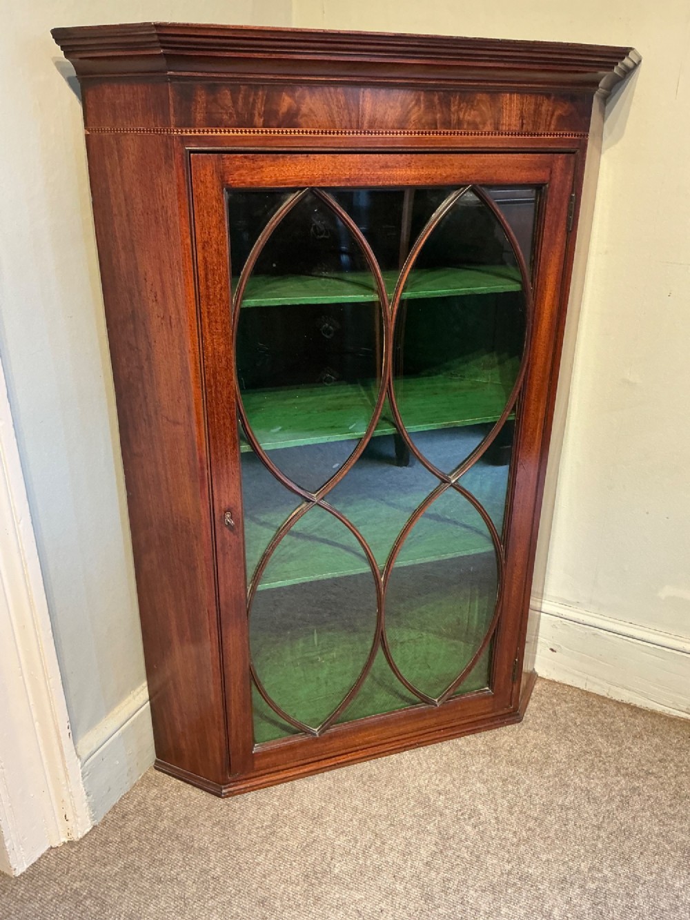 A Georgian mahogany wall-hanging corner cabinet featuring a moulded cornice and a single glass door with geometric oval astragal glazing bars. View III