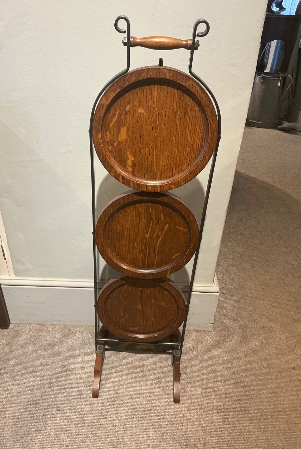 An antique three-tier folding oak cake stand featuring a central turned wooden handle and a dark metal frame.