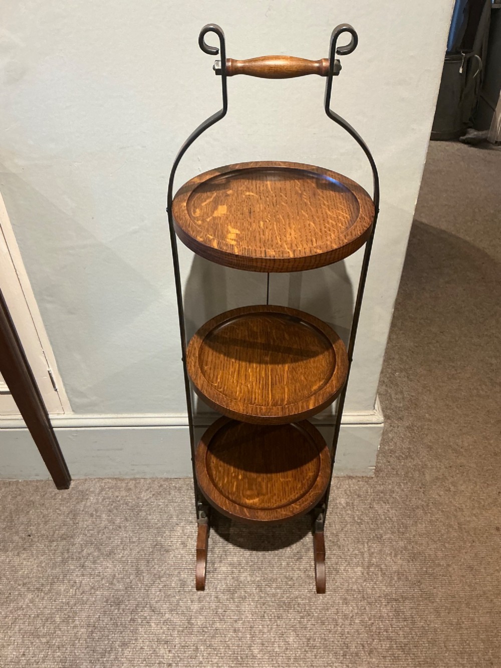 An antique three-tier folding oak cake stand featuring a central turned wooden handle and a dark metal frame. View III