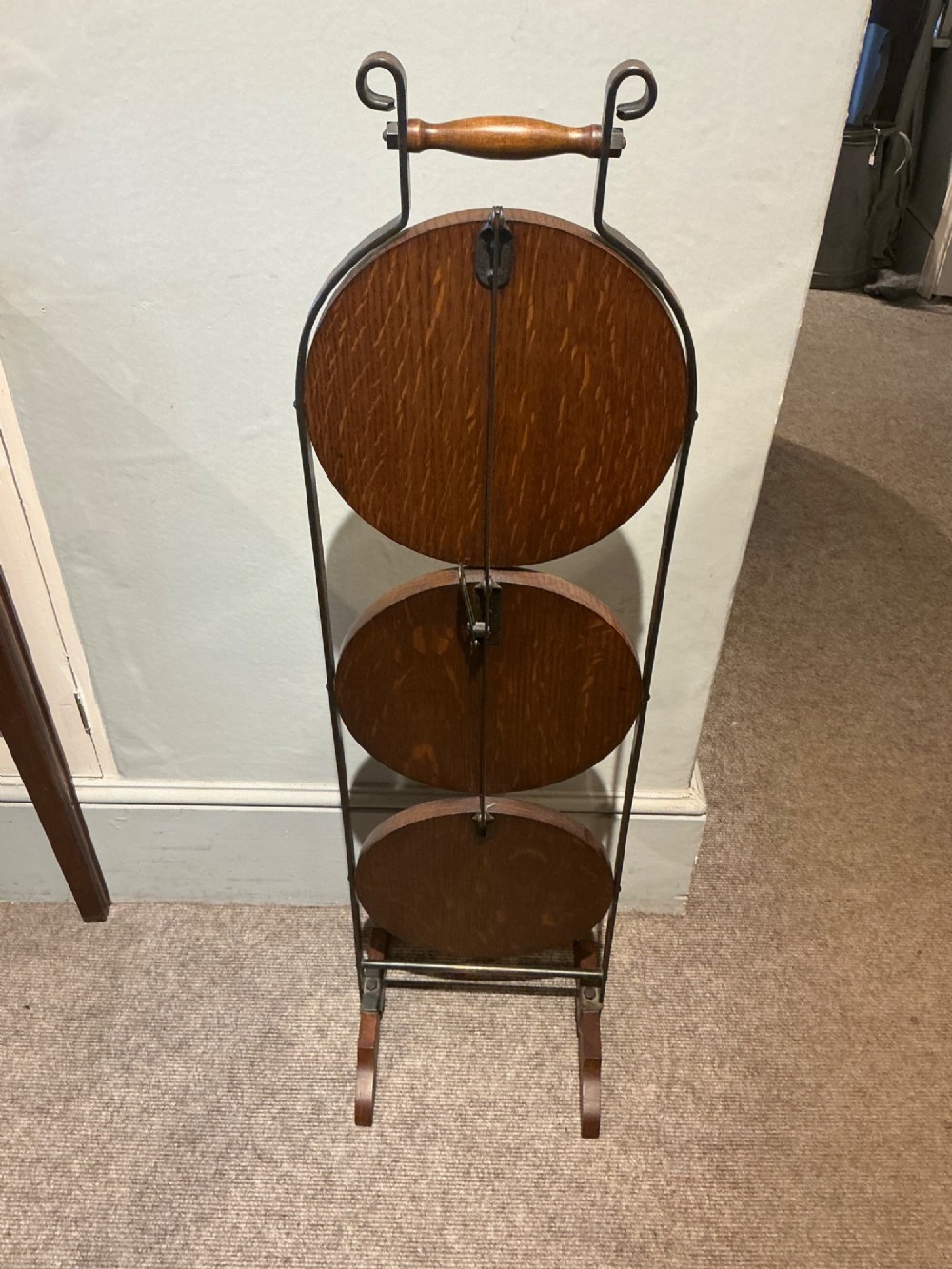An antique three-tier folding oak cake stand featuring a central turned wooden handle and a dark metal frame. View V
