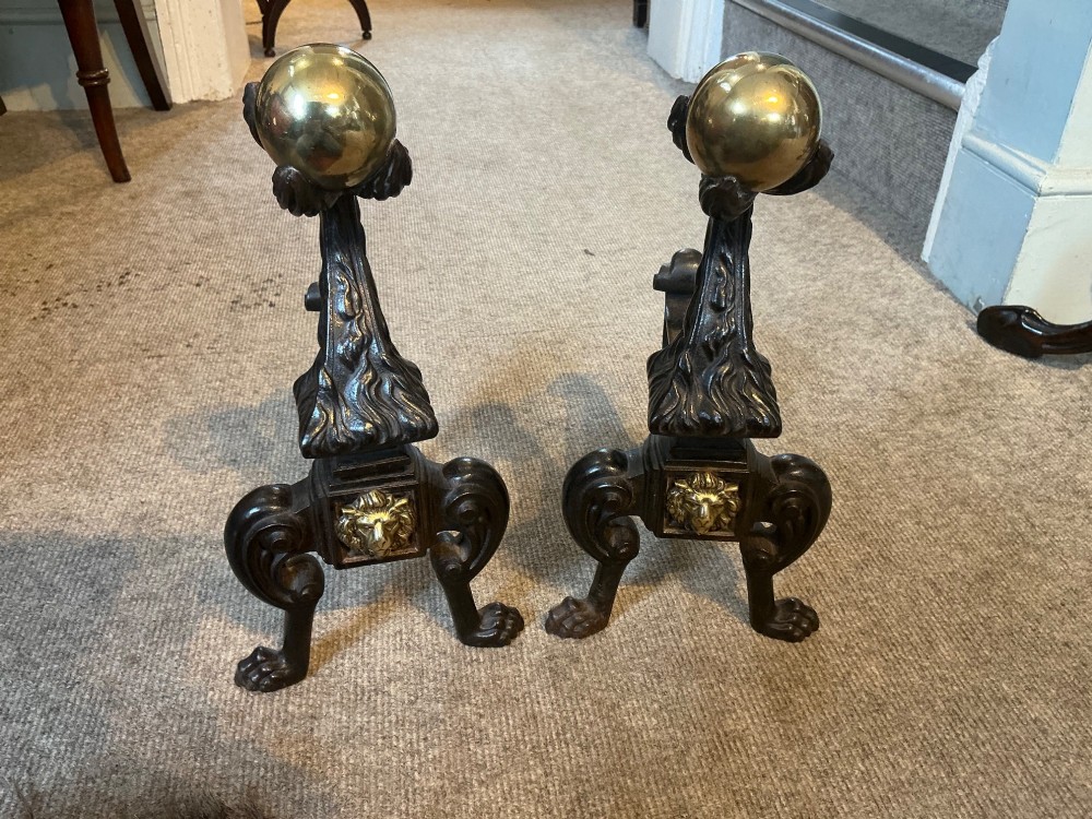 A pair of antique cast iron and brass andirons featuring spherical brass finials, lion mask central motifs, scrolled legs, and claw feet. View II
