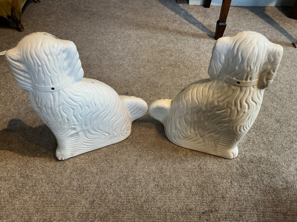 A pair of seated white earthenware Staffordshire spaniel figurines decorated with gold leaf accents and painted black facial features. View II