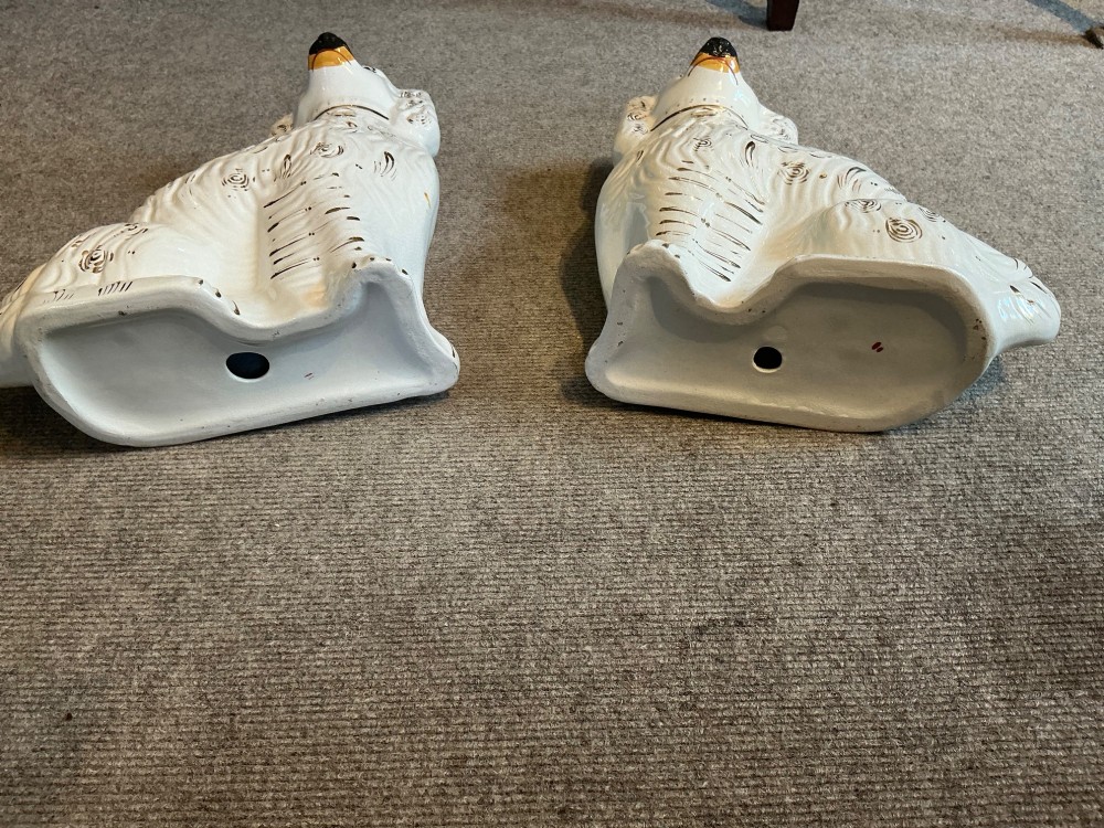 A pair of seated white earthenware Staffordshire spaniel figurines decorated with gold leaf accents and painted black facial features. View III
