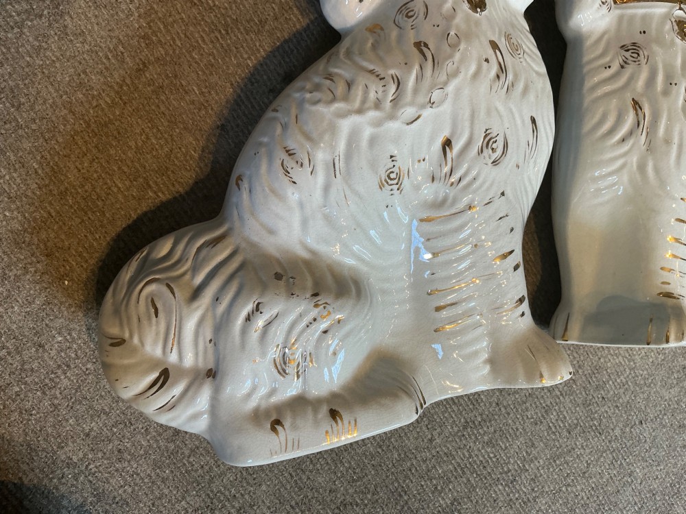 A pair of seated white earthenware Staffordshire spaniel figurines decorated with gold leaf accents and painted black facial features. View V