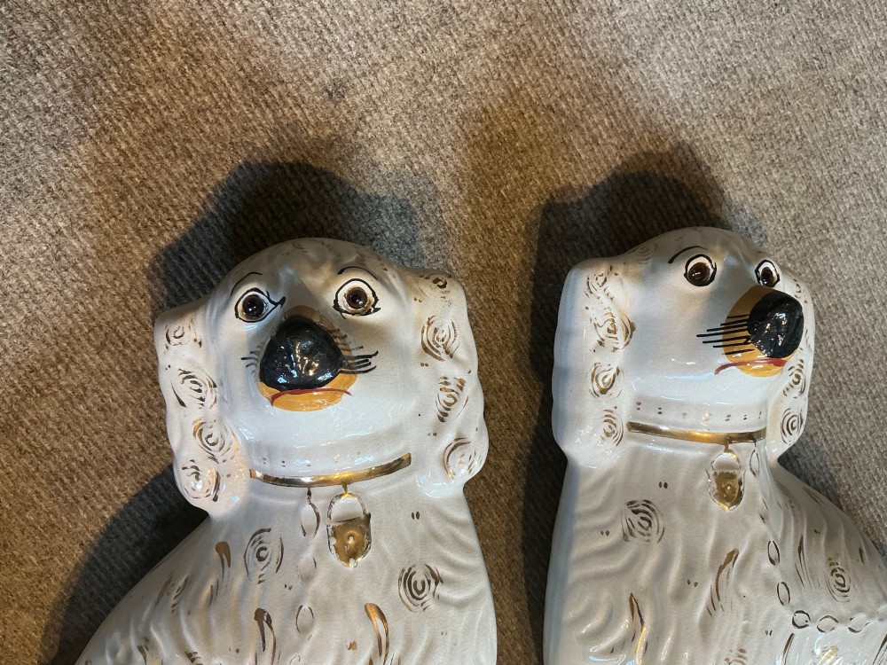 A pair of seated white earthenware Staffordshire spaniel figurines decorated with gold leaf accents and painted black facial features. View VI
