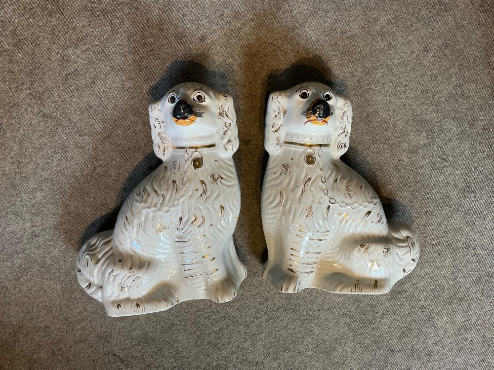 A pair of seated white earthenware Staffordshire spaniel figurines decorated with gold leaf accents and painted black facial features. View VII