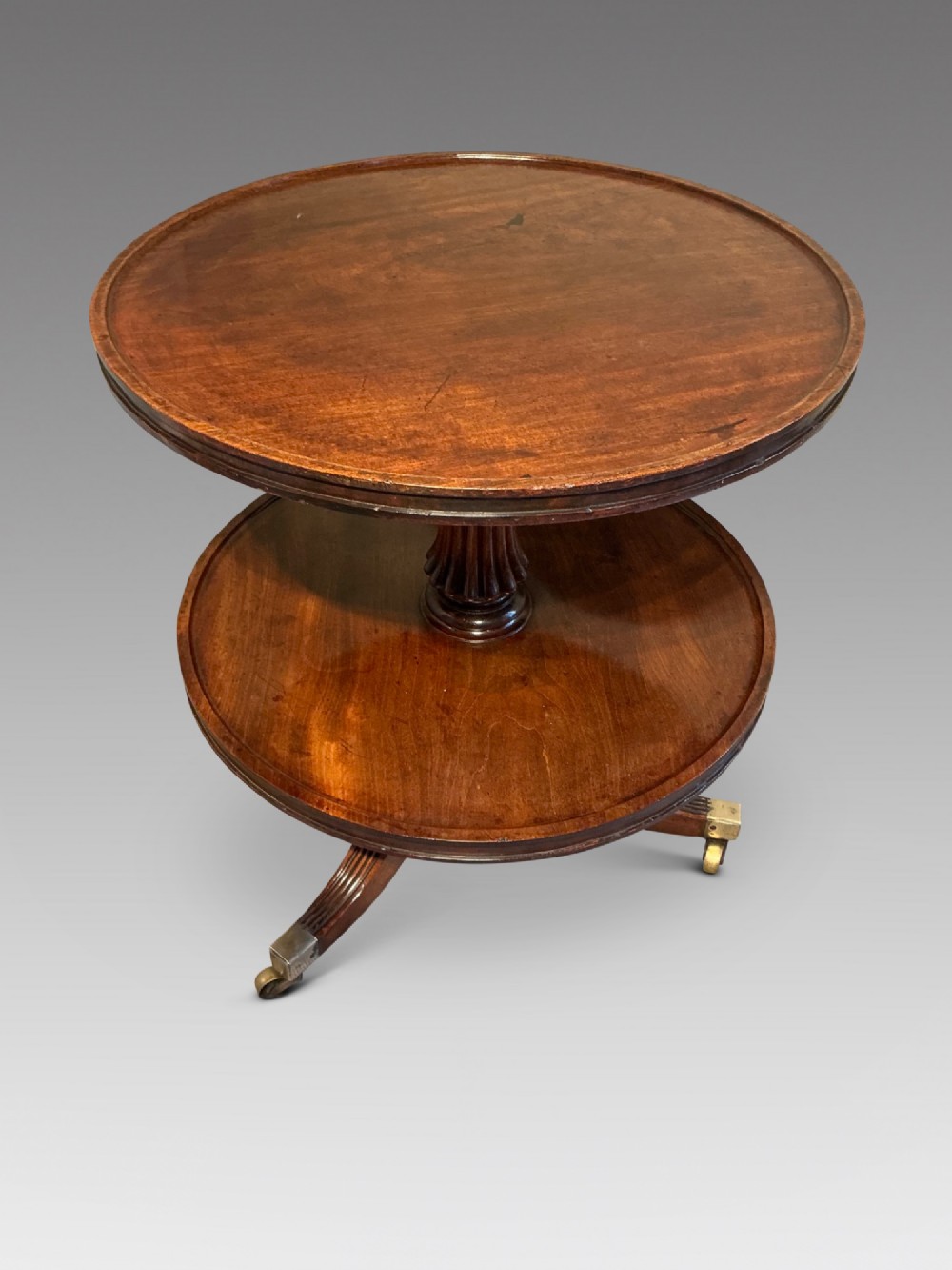 A two-tier dark mahogany Regency dumb waiter featuring a turned central column, reeded tripod legs, and brass castors. View III