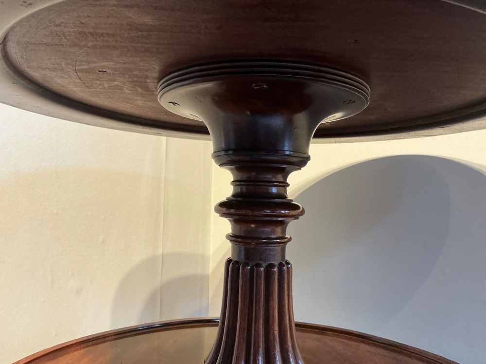 A two-tier dark mahogany Regency dumb waiter featuring a turned central column, reeded tripod legs, and brass castors. View VII
