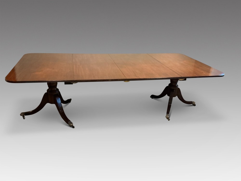 An antique mahogany twin pedestal dining table with rounded corners, extending leaves, turned supports, and splayed legs with brass castors. View II