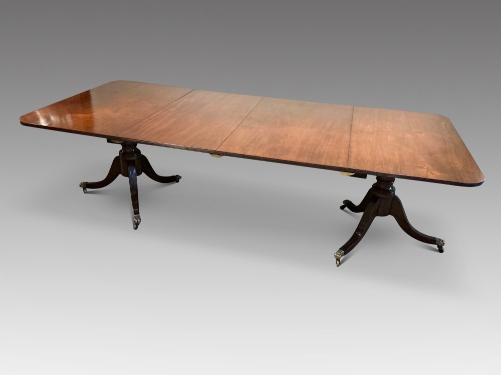An antique mahogany twin pedestal dining table with rounded corners, extending leaves, turned supports, and splayed legs with brass castors. View III