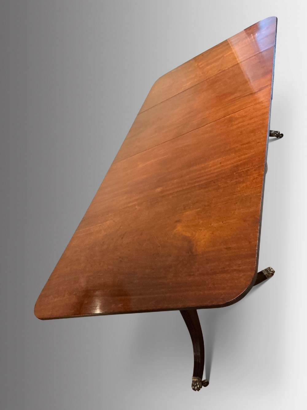 An antique mahogany twin pedestal dining table with rounded corners, extending leaves, turned supports, and splayed legs with brass castors. View IV