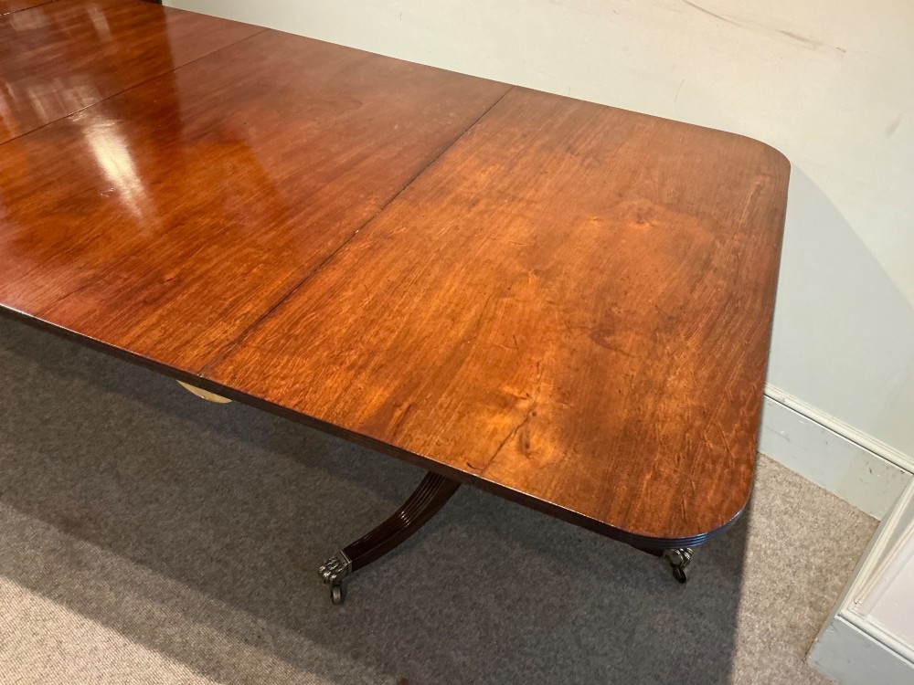 An antique mahogany twin pedestal dining table with rounded corners, extending leaves, turned supports, and splayed legs with brass castors. View V