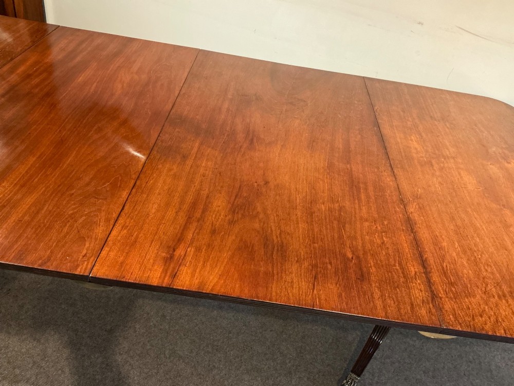 An antique mahogany twin pedestal dining table with rounded corners, extending leaves, turned supports, and splayed legs with brass castors. View VI