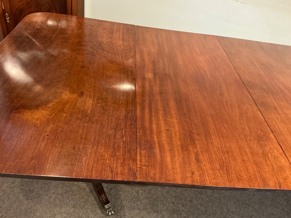 An antique mahogany twin pedestal dining table with rounded corners, extending leaves, turned supports, and splayed legs with brass castors. View VII