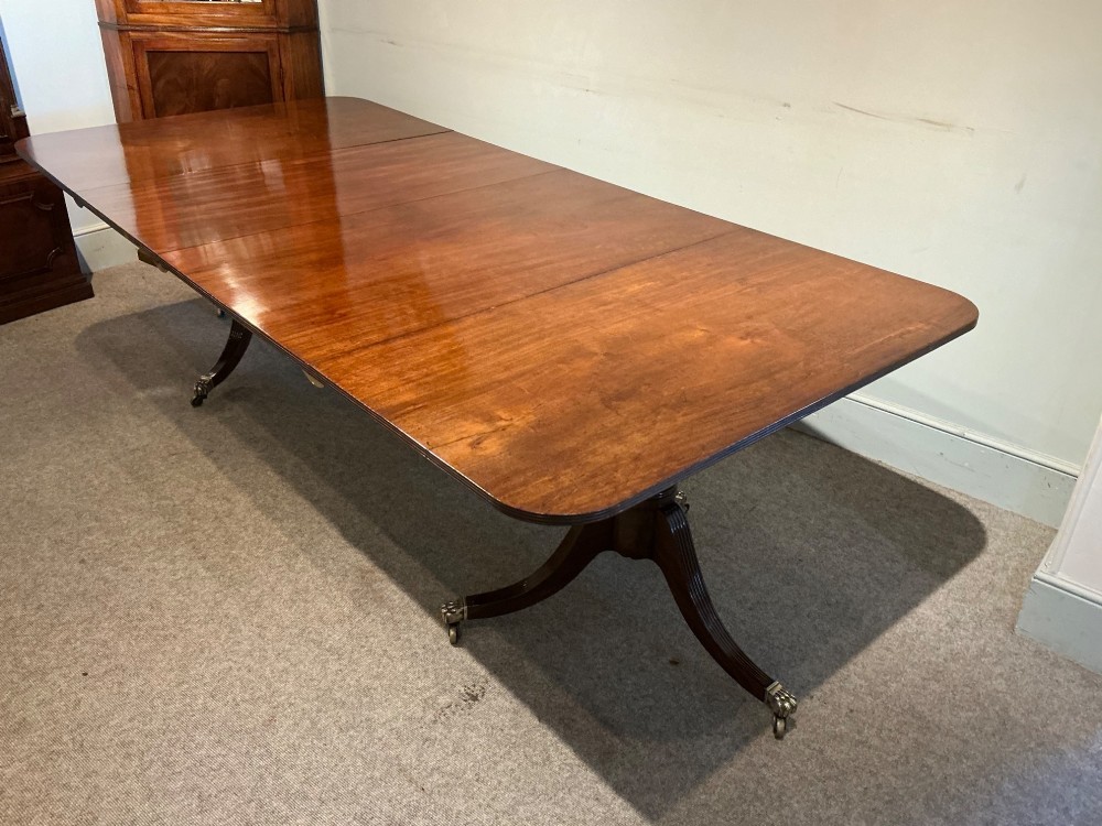 An antique mahogany twin pedestal dining table with rounded corners, extending leaves, turned supports, and splayed legs with brass castors. View VIII