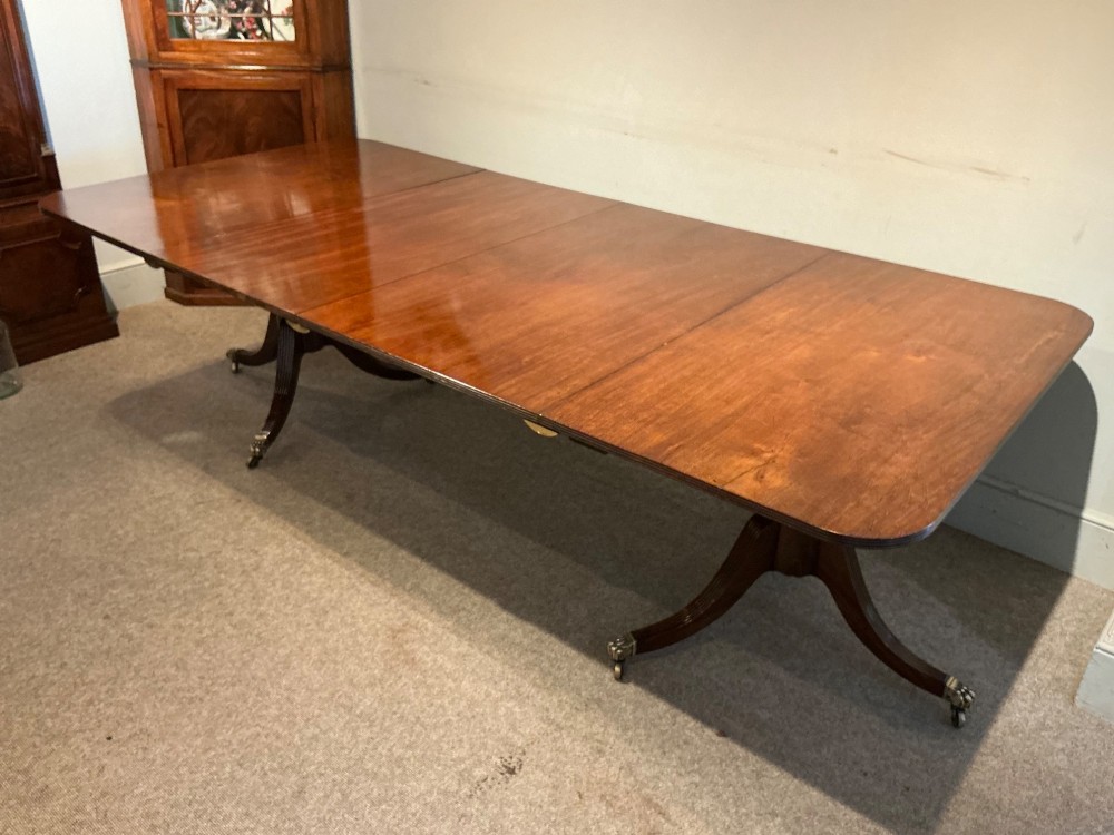 An antique mahogany twin pedestal dining table with rounded corners, extending leaves, turned supports, and splayed legs with brass castors. View IX