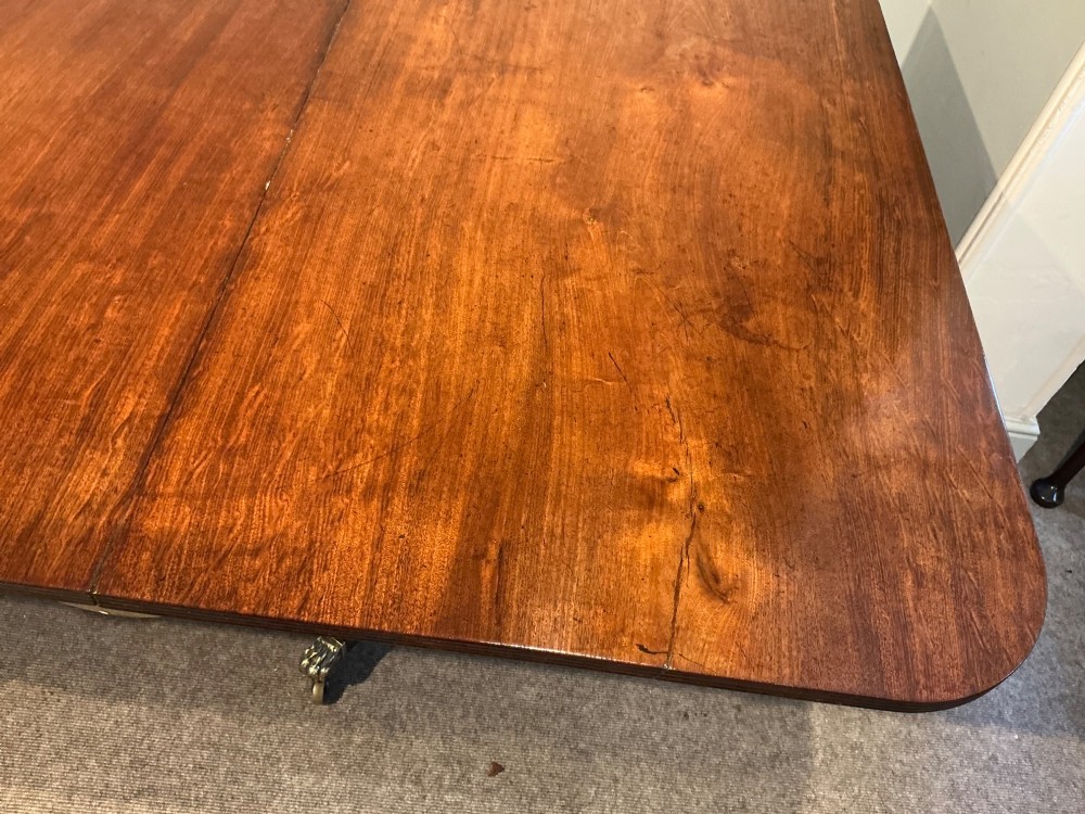 An antique mahogany twin pedestal dining table with rounded corners, extending leaves, turned supports, and splayed legs with brass castors. View X